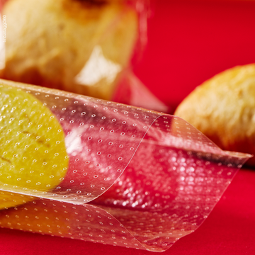 Sacchetto microforato , mostrato con del pane, dentro, anche steso. Dettaglio. Sfondo rosso